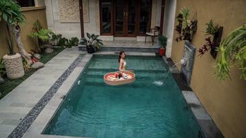 A pool with a floating tray, surrounded by potted plants and a stone pathway.