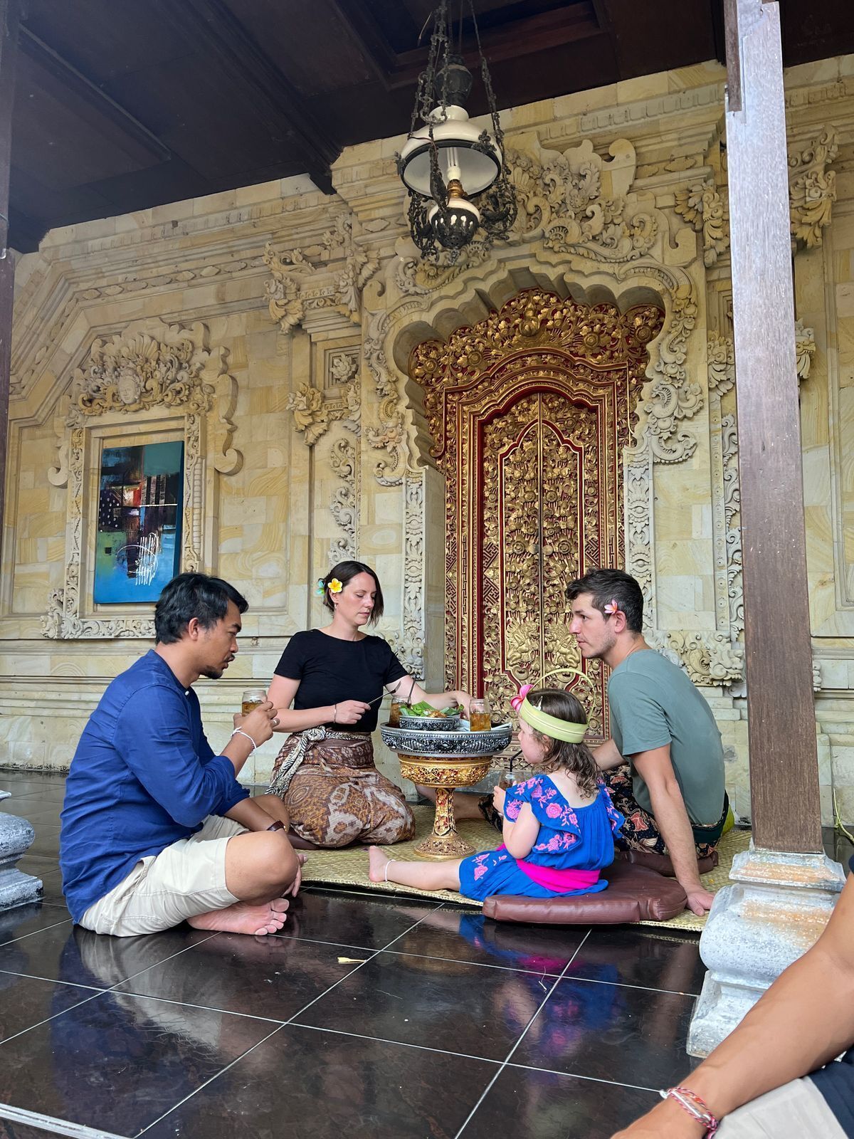 A group of people sitting on the floor in front of an ornate building with intricate carvings and a large, decorative door.