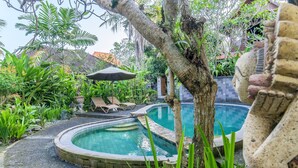 A circular pool with a stone edge, surrounded by lush greenery and a statue. - Sari Bamboo Bungalows (Ubud)