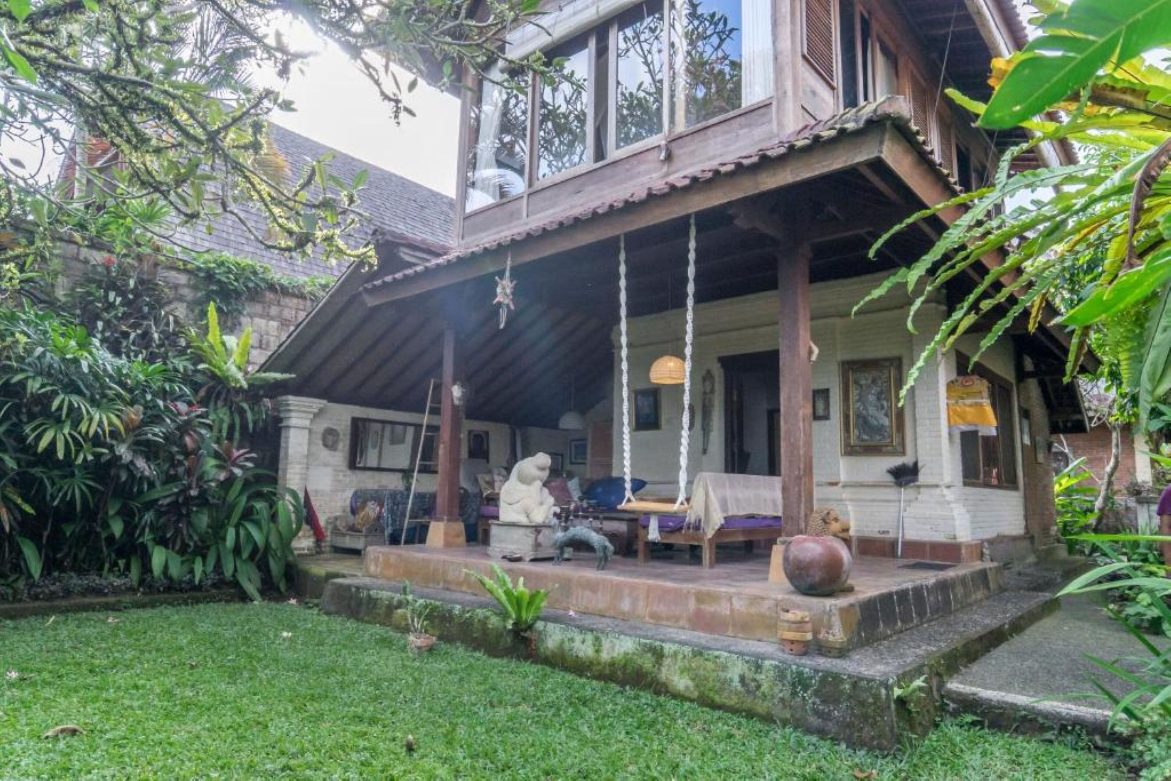 A traditional wooden house with a porch, surrounded by lush greenery.