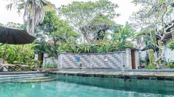 A swimming pool with a tiled edge, surrounded by lush greenery and a stone wall with a statue.
