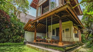 A traditional wooden house with a balcony, surrounded by lush greenery. - Sari Bamboo Bungalows (Ubud)