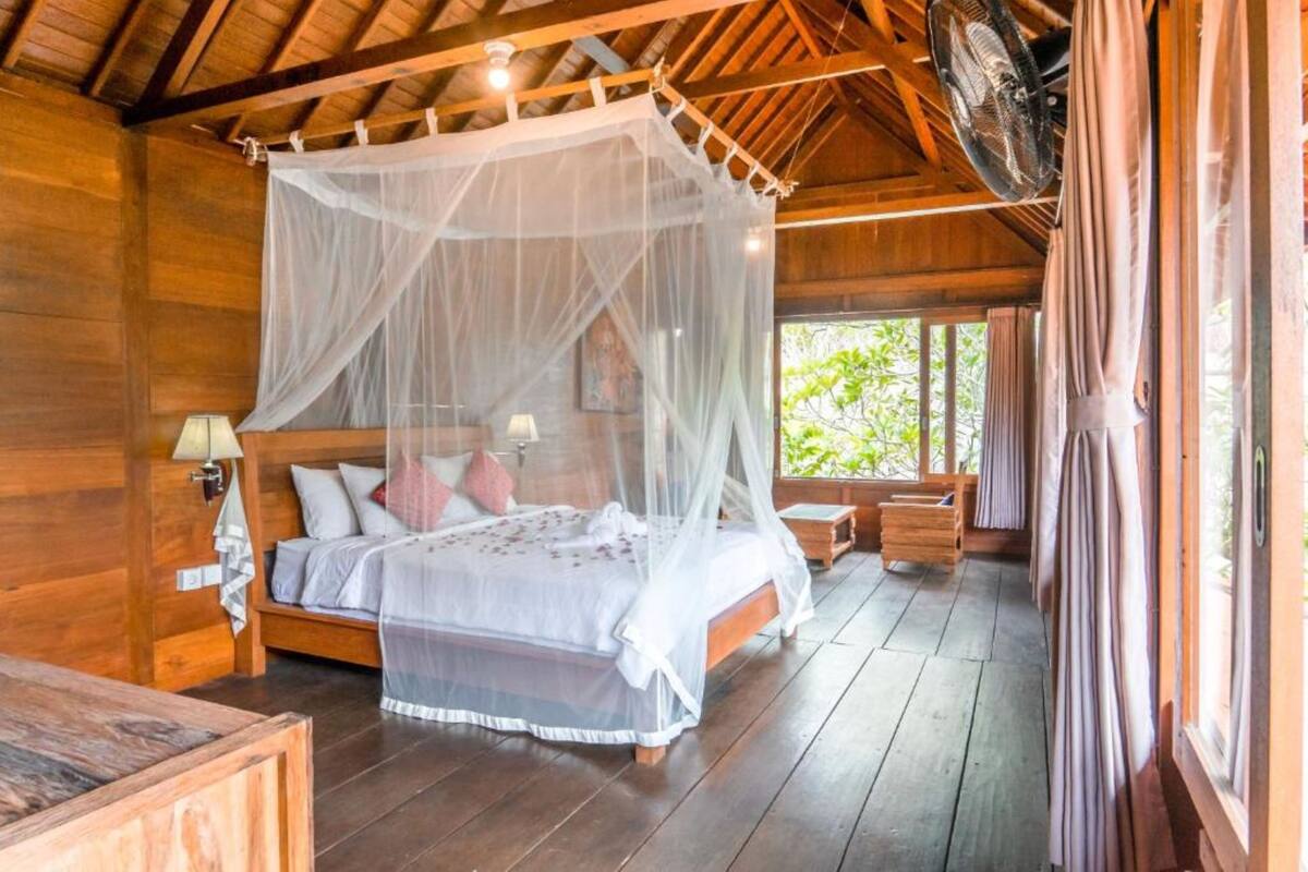 Un dormitorio de cabaña de madera con una cama con dosel, una mesita de noche y un ventanal con cortinas.
