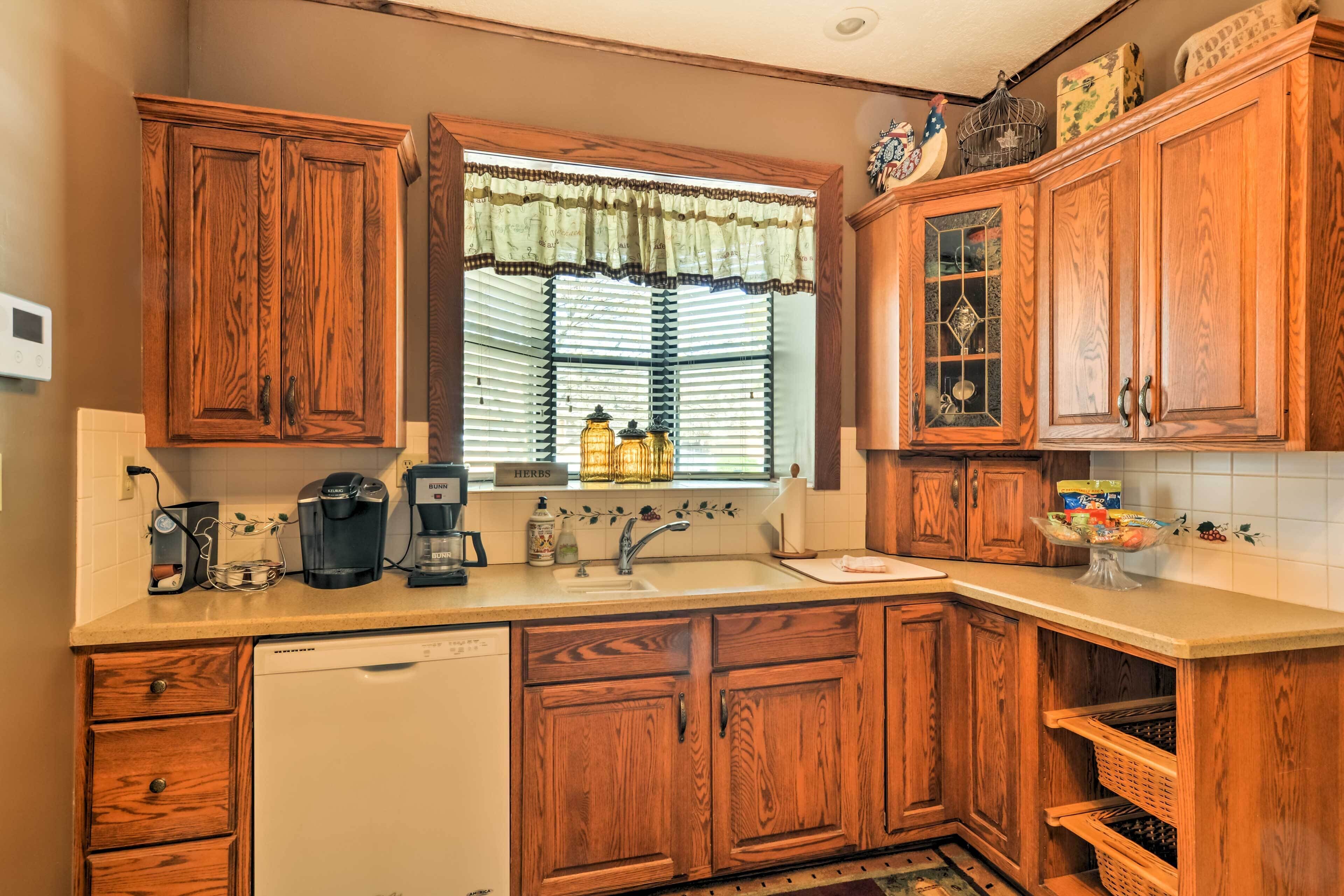 Una cocina con armarios de madera, lavavajillas, cafetera y una ventana con persianas.