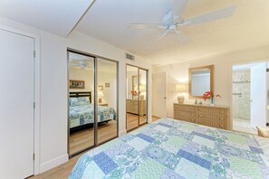 Une chambre avec un grand lit, un placard avec porte coulissante, une salle de bain avec douche et un ventilateur de plafond.