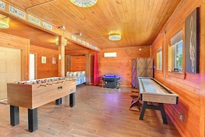 A wooden-floored room with a foosball table, pool table, and a red curtain. - Rim Rock I Blanco, Log Cabin , Pool, Hot Tub, 10 acres of Nature to Explore (Blanco)