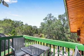 A balcony with a green railing, a metal table, and chairs, overlooking a forested area. - Rim Rock I Blanco, Log Cabin , Pool, Hot Tub, 10 acres of Nature to Explore (Blanco)