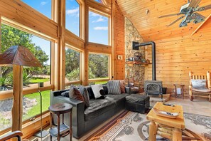 A spacious living area with a large window, a fireplace, and a cozy seating arrangement. - Rim Rock I Blanco, Log Cabin , Pool, Hot Tub, 10 acres of Nature to Explore (Blanco)