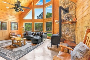 A log cabin interior with a fireplace, wooden furniture, and large windows. - Rim Rock I Blanco, Log Cabin , Pool, Hot Tub, 10 acres of Nature to Explore (Blanco)