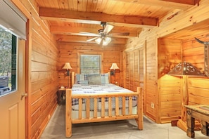A wooden cabin bedroom with a bed, two bedside lamps, a ceiling fan, and a window with blinds. - Rim Rock I Blanco, Log Cabin , Pool, Hot Tub, 10 acres of Nature to Explore (Blanco)