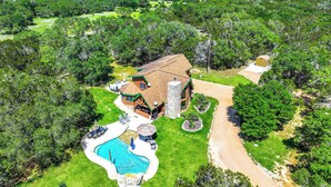 A large house with a swimming pool, surrounded by lush greenery and a clear sky. - Rim Rock I Blanco, Log Cabin , Pool, Hot Tub, 10 acres of Nature to Explore (Blanco)