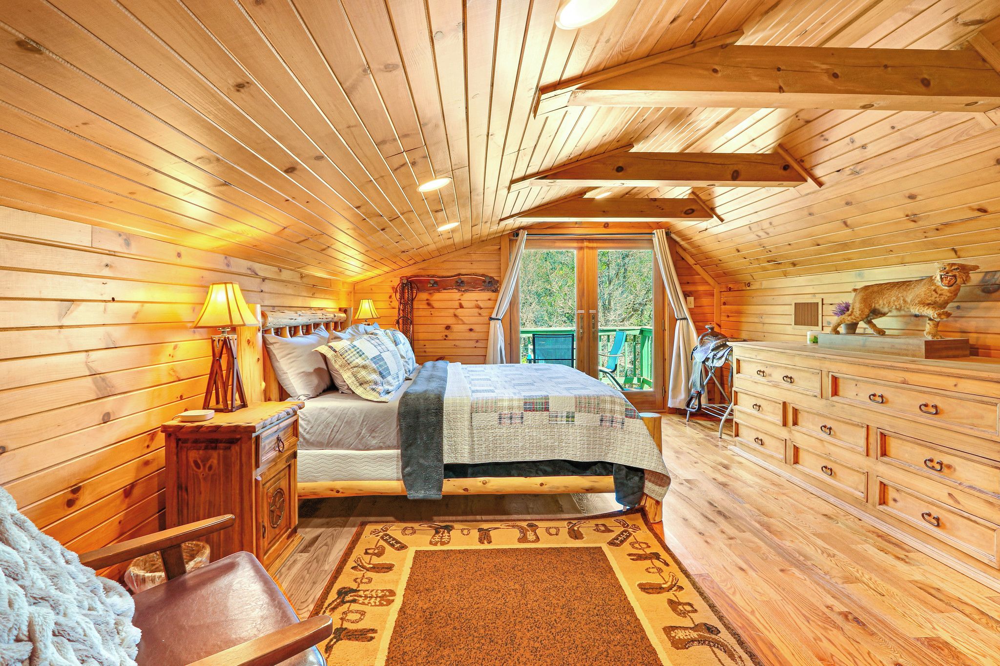 A cozy wooden cabin bedroom with a bed, dresser, and a window overlooking greenery.