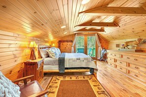 A cozy wooden cabin bedroom with a bed, dresser, and a window with a view of trees. - Rim Rock I Blanco, Log Cabin , Pool, Hot Tub, 10 acres of Nature to Explore (Blanco)