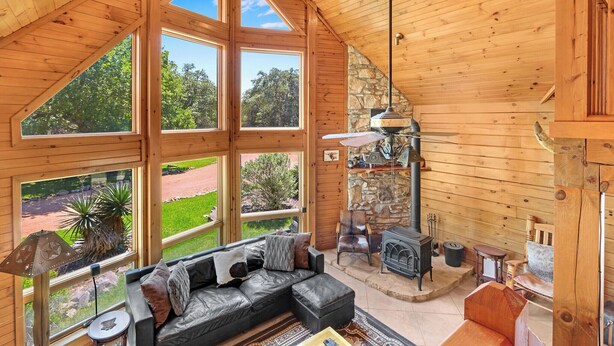A cozy cabin with a large wooden interior, a stone fireplace, and a black leather sofa. - Rim Rock I Blanco, Log Cabin , Pool, Hot Tub, 10 acres of Nature to Explore (Blanco)
