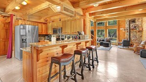 A spacious kitchen with wooden cabinets, a stainless steel refrigerator, a microwave, and a stone accent wall. - Rim Rock I Blanco, Log Cabin , Pool, Hot Tub, 10 acres of Nature to Explore (Blanco)