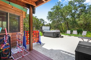 An outdoor patio with a hot tub, seating area, and children's play equipment. - Rim Rock I Blanco, Log Cabin , Pool, Hot Tub, 10 acres of Nature to Explore (Blanco)