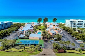 Un resort con varias construcciones, una cancha de tenis y vista al océano.