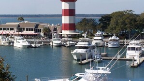 Un port de plaisance avec un phare rouge et blanc bien visible, plusieurs yachts amarrés et un restaurant en bord de mer doté d’une terrasse.