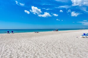 A beach with white sand and clear blue water. There are blue lounge chairs and umbrellas.