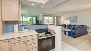 Una cocina moderna con horno y estufa integrados, un rincón comedor con sofá azul y vistas al exterior.