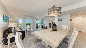 A spacious dining area with a large wooden table and benches, a hanging light fixture, and a view of the outdoors. - Unit #117 Sand Cay Beach Resort Gulf Front (Longboat Key)