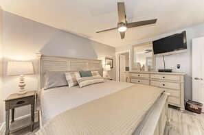 A bedroom with a bed, nightstands, a dresser, a ceiling fan, a TV mounted on the wall, and a mirror.