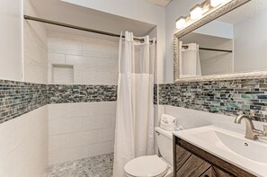A bathroom with a shower curtain, a toilet, a sink with a mirror, and a tiled backsplash.