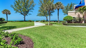 A well-maintained outdoor area with a pathway, manicured lawn, and several trees. - Unit #117 Sand Cay Beach Resort Gulf Front (Longboat Key)