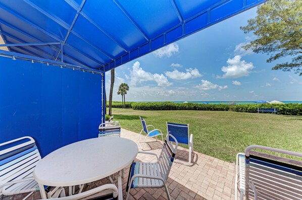 An outdoor patio with a blue canopy, a round table, and metal chairs.