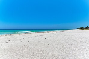 A wide sandy beach with clear blue water and a distant shoreline.