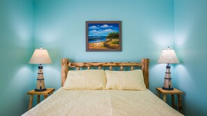 Een bed met een houten hoofdeinde, twee bedlampjes en een schilderij van een strand.