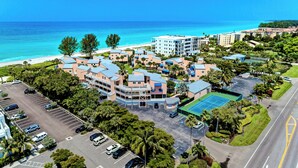 A coastal hotel with multiple buildings, a parking lot, and a tennis court.