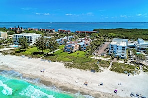 An aerial view of a coastal resort with beachfront properties, a sandy beach, and ocean views. - Unit #107 Sand Cay Beach Resort Pool View (Longboat Key)