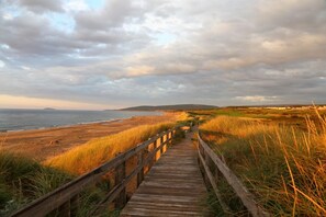 A wooden boardwalk leading to a beach with grassy dunes and a cloudy sky.