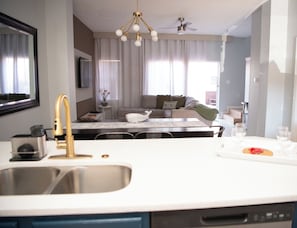 A modern kitchen with a sink, a dishwasher, a dining area with a table and chairs, a sofa, and a ceiling fan.