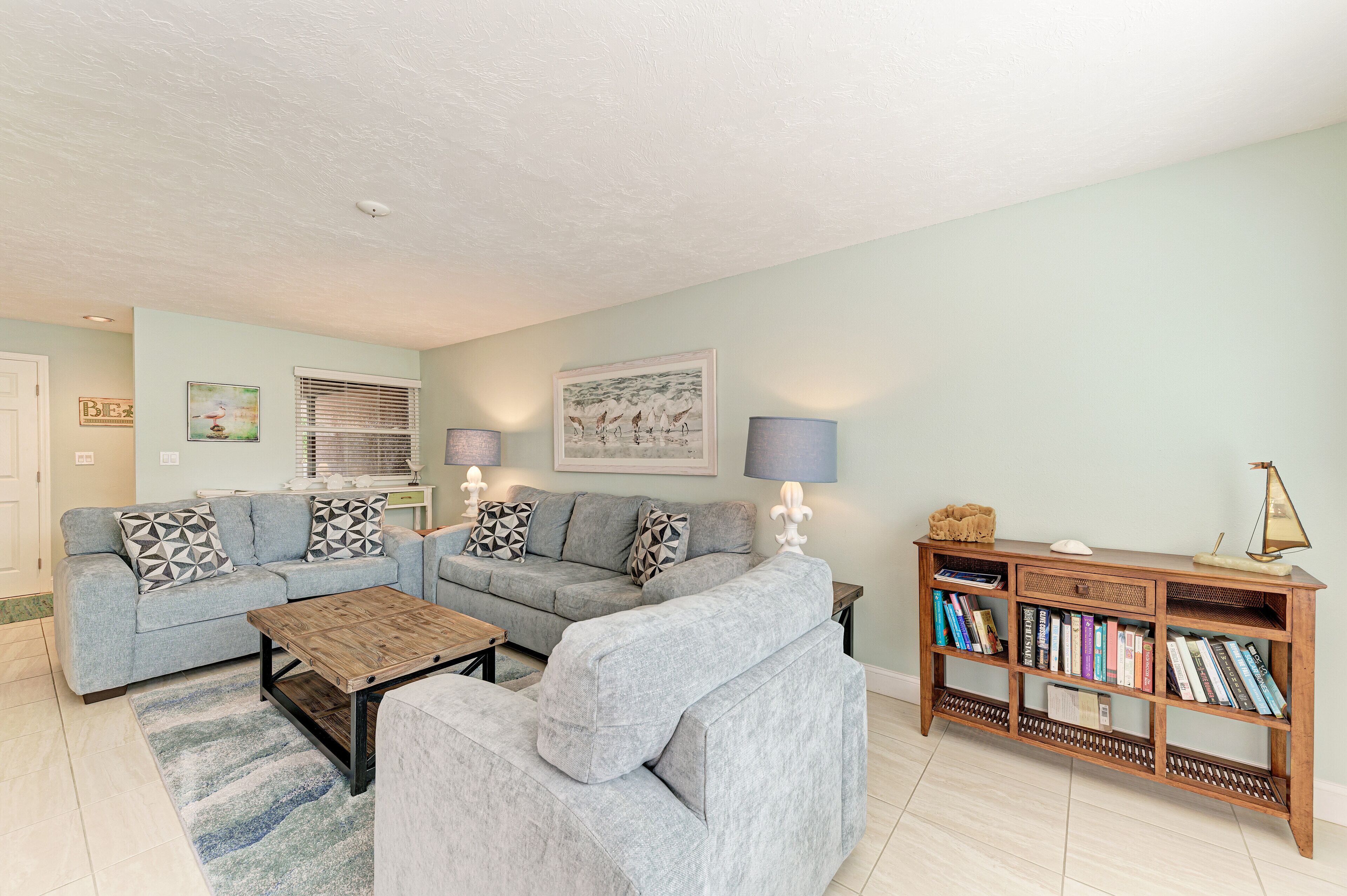 A living room with two grey sofas, a wooden coffee table, a bookshelf, and a framed picture on the wall.