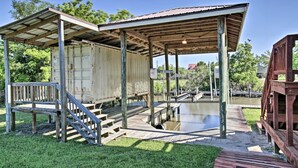 A covered wooden structure with a metal roof, a wooden staircase, and a dock extending into a body of water. - Private Dock w/ Lift: Waterfront New Orleans Home! (New Orleans)