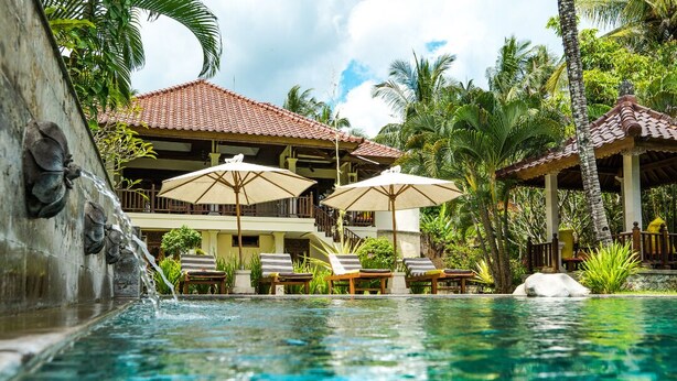 A pool area with lounge chairs and umbrellas, surrounded by tropical vegetation and a building with a tiled roof. - Bali's Finest, Luxurious Villa Tunjung with Private Pool&Staff in Unspoiled Bali (Seririt)