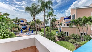 Un resort con diversi edifici, palme e una piscina con lettini e ombrelloni.