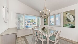 Un coin repas avec une table en verre, des chaises en osier blanc, un lustre et des œuvres d’art accrochées aux murs.