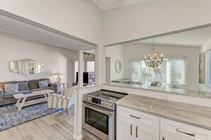 A modern kitchen with a built-in oven, a large island with a sink, and a dining area with a sofa and a coffee table. - Unit #311 Sand Cay Beach Resort Pool View (Longboat Key)