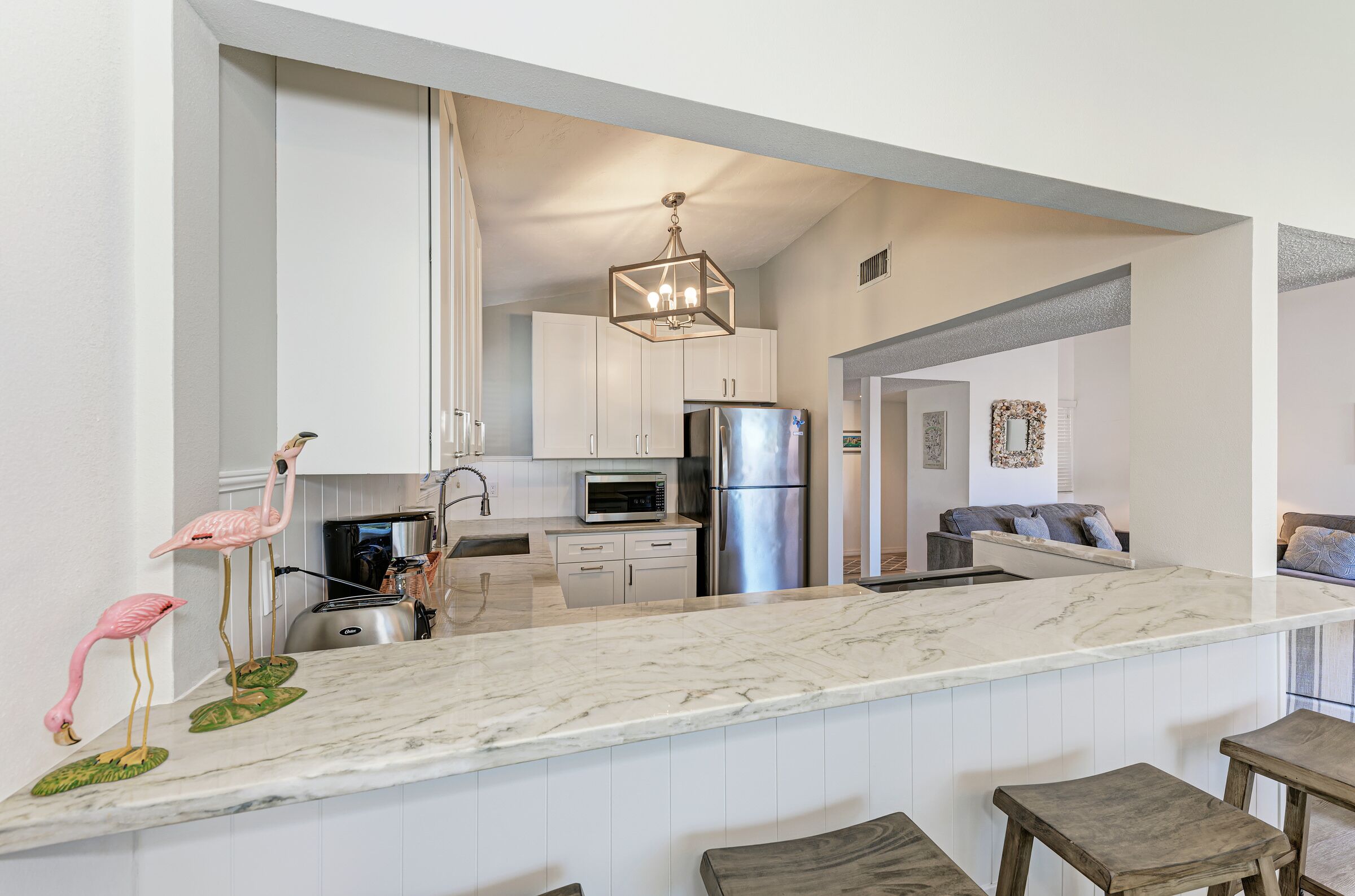 Una cocina moderna con gabinetes blancos, encimera de mármol y refrigerador de acero inoxidable.