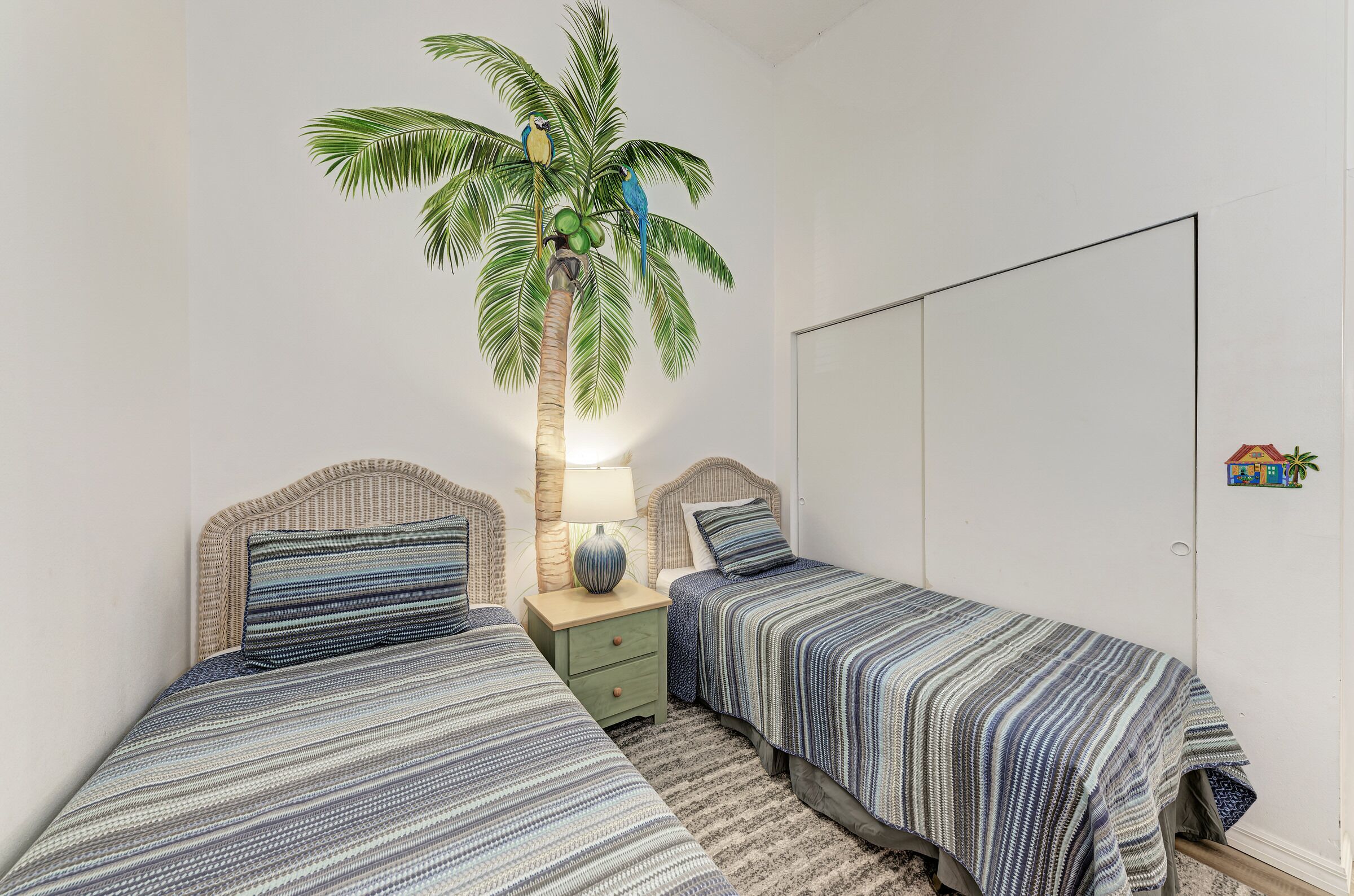 Ein Schlafzimmer mit zwei Betten, einem Nachttisch, einer Lampe, einem an der Wand montierten Fernseher und einer Zimmerpflanze als Dekoration.