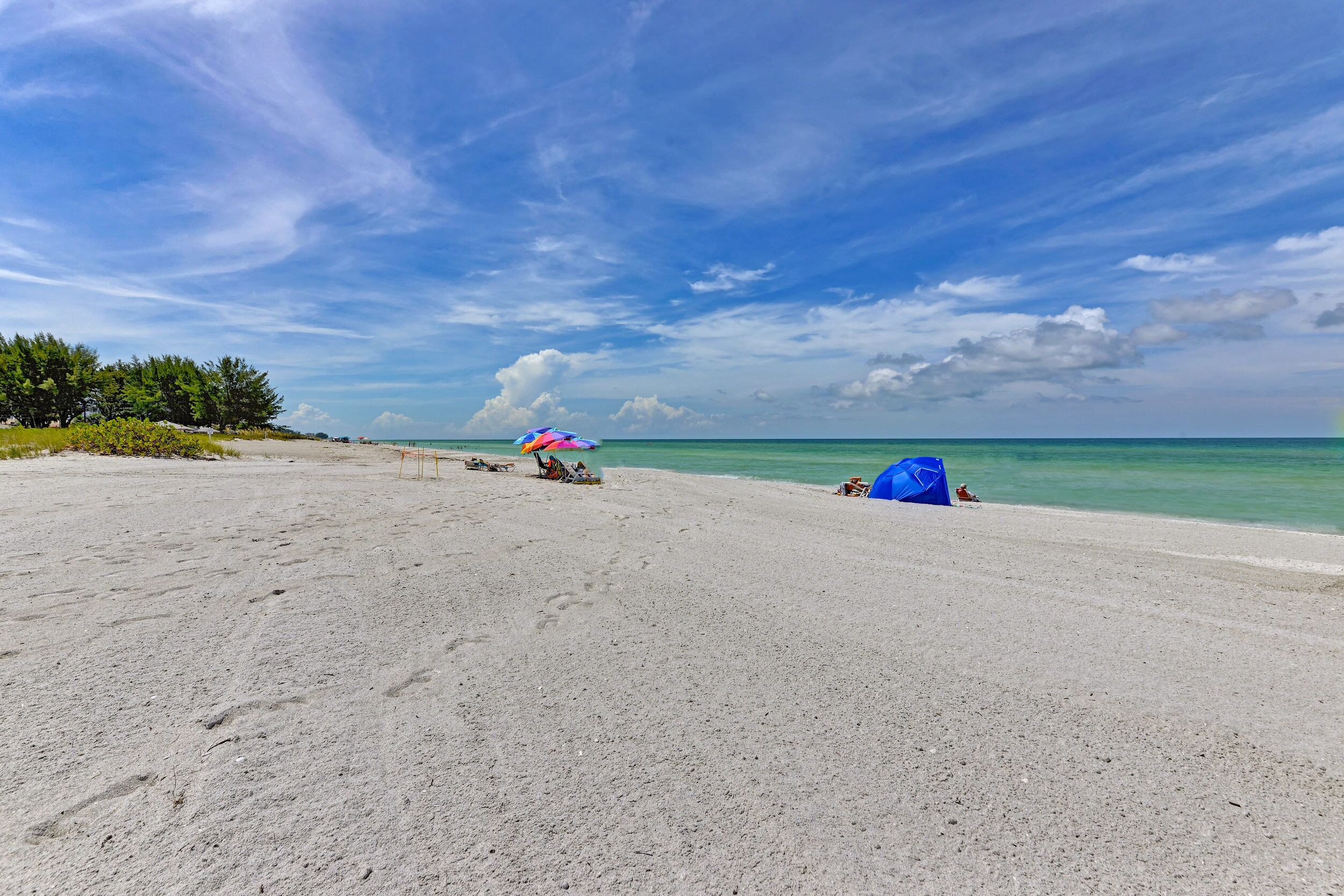 A beach with a clear sky, a few umbrellas, and a tent.