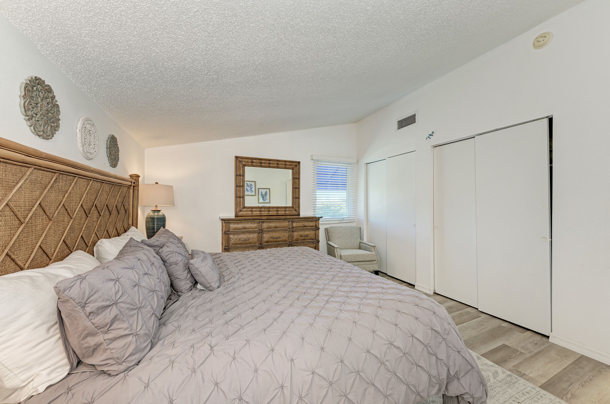 Een slaapkamer met een groot bed, een houten hoofdbord, een dressoir, een stoel en een kledingkast.