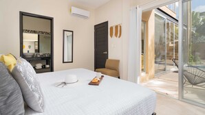 Quarto de hotel com uma cama, uma cadeira, uma mesinha com bandeja, um espelho e uma porta de vidro deslizante para uma área externa.