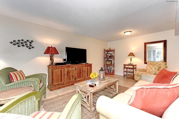 A living room with a television, wooden cabinet, wicker chairs, a patterned sofa, and a decorative mirror. - Unit #108 Sand Cay Beach Resort Pool View (Longboat Key)