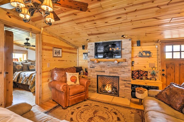 Interior acogedor de una cabaña de troncos con chimenea, muebles de cuero y una pared de piedra.
