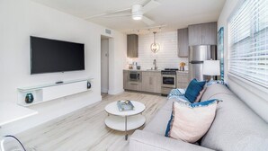 En moderne stue med et fladskærms-TV, et glasbord og en grå sofa.