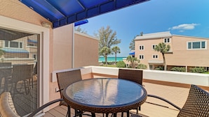 A balcony with a round table and chairs, a glass door, and a view of a building and palm trees. - Unit #215 Sand Cay Beach Resort Gulf View (Longboat Key)